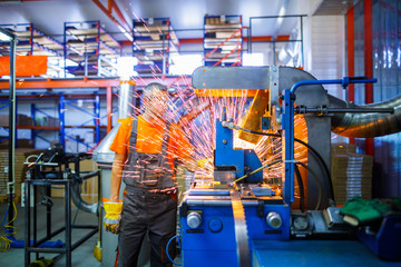 Naklejka premium A male mechanic working on welding machine in the Industrial production of metal products. Sparks fly out of under the parts. Concept theme repair, mechanics, production, industry. Unrecognizable face
