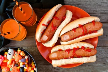 Obraz premium Halloween meal scene with hot dog fingers, drinks and candy, above view a wood background