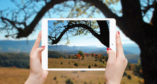 Girl taking photo with tablet of colorful autumn trees and hills