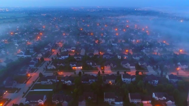 Tranquil urban neighborhoods still asleep under foggy twilight, aerial view.
