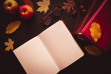 Back to school concept. Open notebook top view on the pile of books lying on the black chalkboard