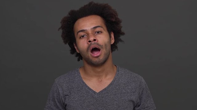 African American young male yawning isolated on charcoal background. Concept of emotions