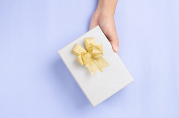 Silver gift box with golden ribbon in hand for giving in holidays