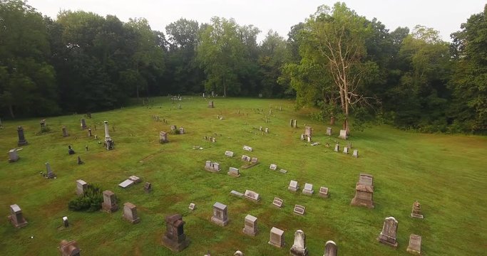 A forward high angle aerial above a historic cemetery in the woods.  	