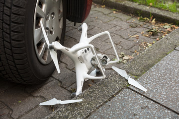 Broken drone by car wheel on footpath