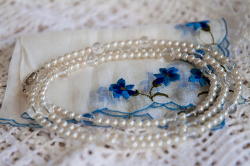 White and clear beaded necklace placed on top of an old-fashioned handkerchief and a crochet doily