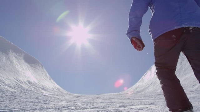 SLOW MOTION: Young pro snowboarder walking uphill in the halfpipe snow park carrying his board on a beautiful sunny day in snowy winter