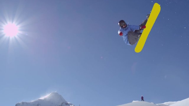 SLOW MOTION: Young pro snowboarder riding the half pipe in big mountain snow park, jumping high out of the halfpipe wall, performing tricks and rotations with grabs in sunny winter 