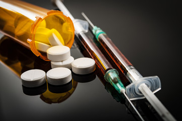 Opioid epidemic, drug abuse concept with closeup on two heroin syringes or other narcotics surrounded by scattered prescription opioids. Oxycodone is the generic name for a range of opioid painkillers