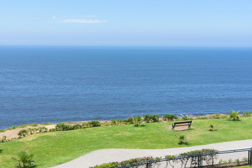 Fototapeta na wymiar empty bench facing towards the ocean coast against blue sky
