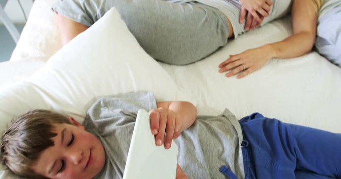 Siblings using digital tablet while parent sleeping in bedroom 