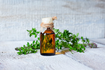 Thyme oil skincare. Bottle of herbal extract, aromatic fresh green twigs, soft focus on wooden bacground