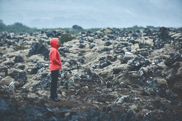 Obraz premium Woman in waterproof clothing walks on volcanic Lava fields on background of mountains of Iceland.