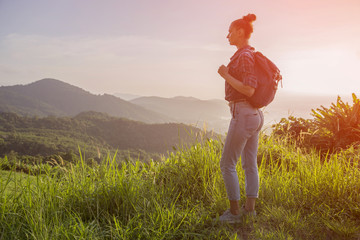 Hipster young girl with backpack enjoying sunset on peak of foggy mountain. Tourist traveler on...