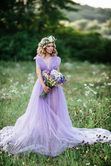 Fototapeta na wymiar beauty woman portrait with wreath of flowers on head. bride in purple dress with bouquet of wildflowers .Outdoor. soft focus
