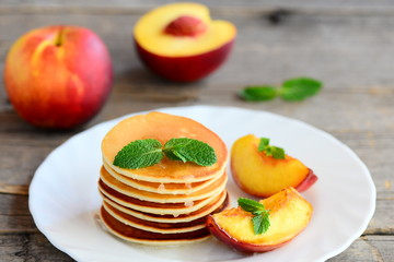 Basic pancakes with syrup and grilled nectarines on a serving plate and an old wooden table. Pancake recipe without butter. Healthy and easy breakfast for kids