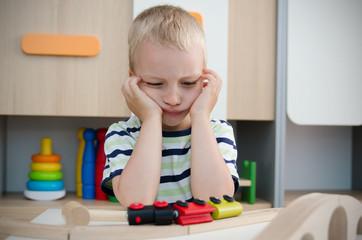 Bored sad little boy sitting at table