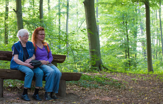an old woman is sitting with her daughter on a bench in the forest