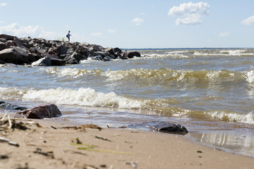 Fototapeta na wymiar ocean waves lapping on the sandy shore, away girl standing on the rocks
