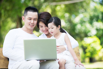 Young happy Asian family looking at the computer together at the park.