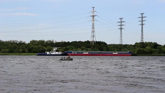 A man on a rubber boat with oars crosses the river, in the background the ship is moving.