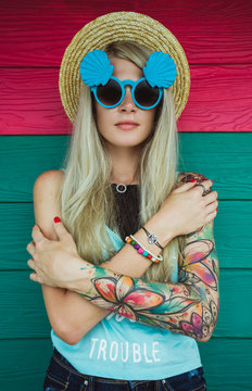 Beautiful young woman hipster with a tattoo in sunglasses and a hat on a bright coloured background. Beach style