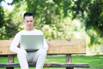 Fototapeta premium Young Asian Man Sitting on a Bench with a Laptop