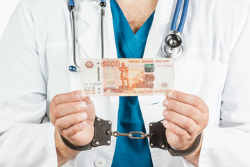 Doctor with a stethoscope and 5000 banknotes and handcuffs. a crime. on a white background.