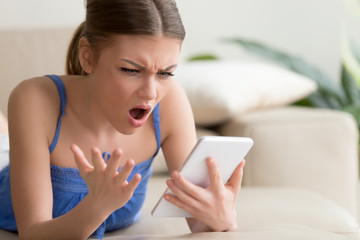 Young woman feeling shocked and looking with confusion on digital tablet screen while browsing...