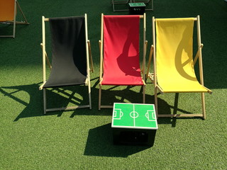 Sommer und Sonnenschein mit Liegestühlen in Schwarz, Rot, Gold auf grünem Kunstrasen einer...