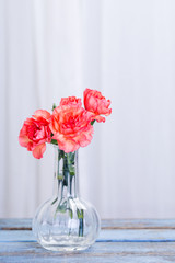 blombukett med orangea nejlikor i glas vas stående på ett blått slitet trä bord med vita gardiner bakom