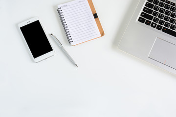 White office desk table with Laptop, notebook and mobile. Top view with copy space.