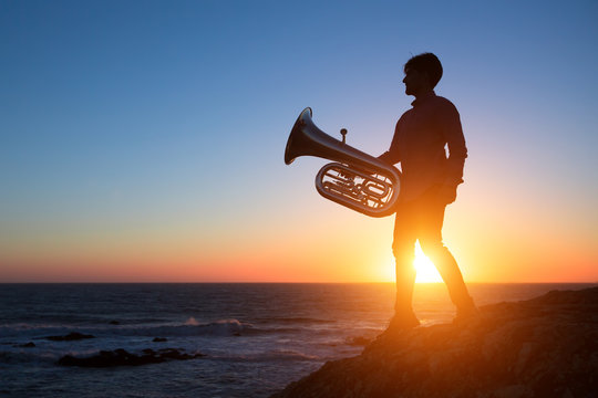 Silhouette of musician with Tuba on sea shore at sunset .