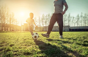 Foto op Plexiglas Father and son playing together with ball in football under sun © Andrii IURLOV