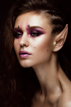 Brunette girl with a creative hairstyle braids, art make-up and the elf's ears. Beauty face. Photo taken in the studio.