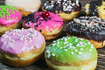assorted doughnuts in the glaze and colorful sprinkles on wooden background