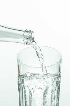 Pouring water from bottle into glass on white