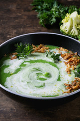 Vegetarian broccoli cream soup served in black bowl with cream, fried onion, fresh parsley and broccoli over old wooden background. Close up. Healthy eating.