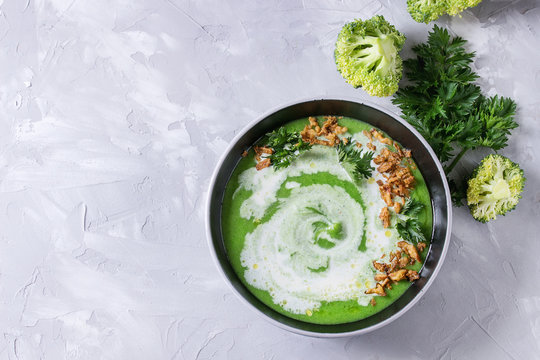 Vegetarian broccoli cream soup served in black bowl with cream, fried onion, fresh parsley and broccoli over over gray concrete background. Top view with space. Healthy eating.