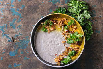 Mushroom cream soup in black ceramic bowl served with turmeric powder, forest mushrooms, greens parsley, fried onion over old dark wooden background. Top view