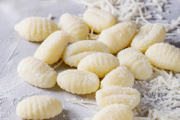 Raw uncooked potato gnocchi with flour and grated parmesan cheese over gray concrete background. Close up. Home cooking.