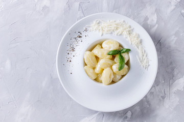 White plate of hot creamy potato gnocchi served with black pepper, grated parmesan and fresh basil over gray concrete background. Flat lay with space