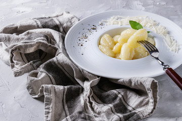 White plate of hot creamy potato gnocchi served with black pepper, grated parmesan, fresh basil, fork on textile napkin over gray concrete background. Close up