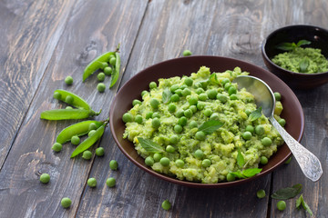 Mashed potatoes with green peas, mint and olive oil in a ceramic bowl on a wooden table. Healthy vegetarian food