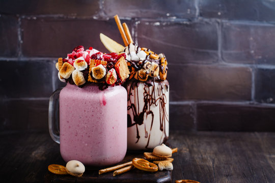 Vanilla and raspberry extreme milkshakes with bretzels, popcorn, small marshmallows, cookies and berries on white background. Copy space