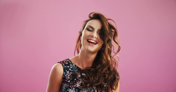 Smiling woman waving hair against pink background 