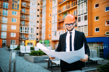 Engineer in front of modern building with plan looking at blueprint