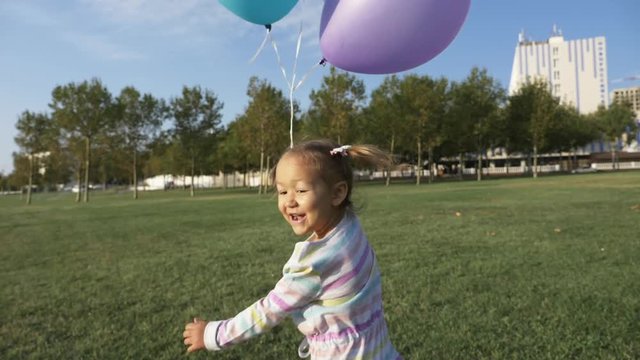 Cute little girl running with balloons in the park and laughing