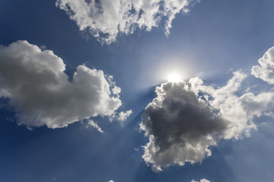 Rays Of Sun Shining Through White Puffy Clouds And Blue Sky