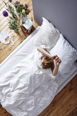 Fototapeta na wymiar young woman waking up stretching herself in bed view from above